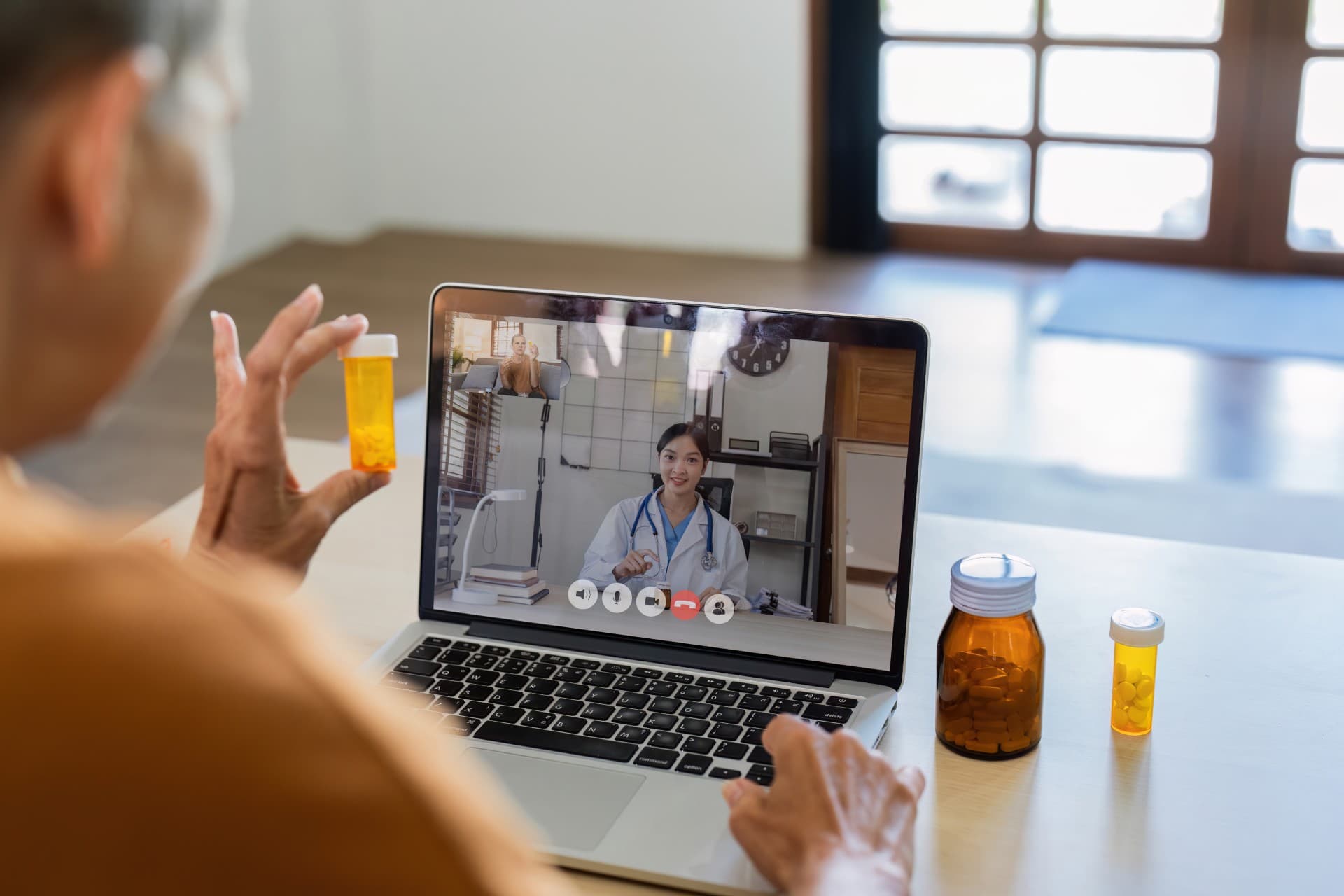 patient on a laptop video visit, holding medication bottles
